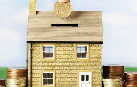 Woman-putting-pound-coin-in-model-house-money-box
